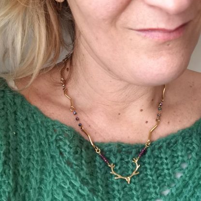 Zoom sur le collier à tête de cerf monté sur chaine articulée, plaquée or et pierres de grenat.