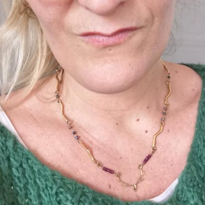 Collier à tête de cerf monté sur chaine articulée, plaquée or et pierres de grenat. Porté.